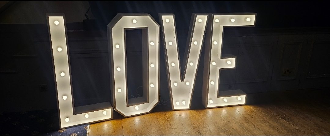 Large illuminated LOVE letters lit with bulbs standing against a wall in a wedding venue