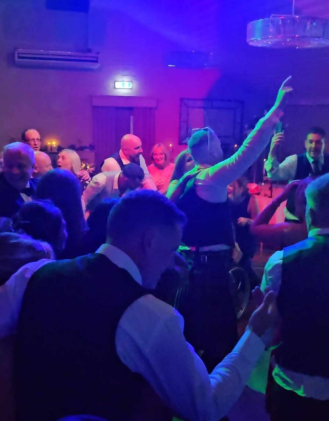 Packed wedding dancefloor with guests singing along under blue and green lighting