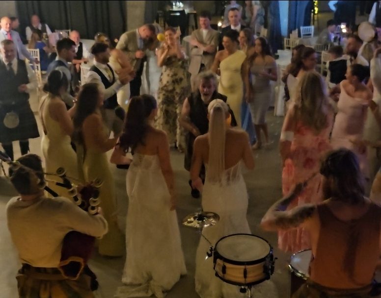 Bagpiper and drummer playing to wedding guests gathered in a circle at a Scottish reception