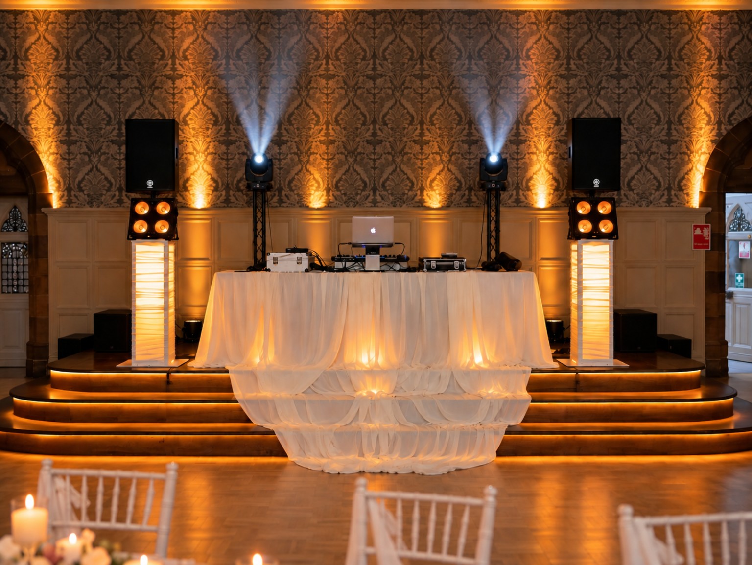 JMD Entertainments wedding DJ setup with warm amber venue lighting, clean white beams and a white-draped booth
