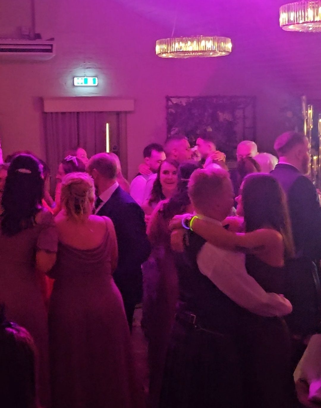 Couples slow dancing in a wedding function room washed in pink uplighting