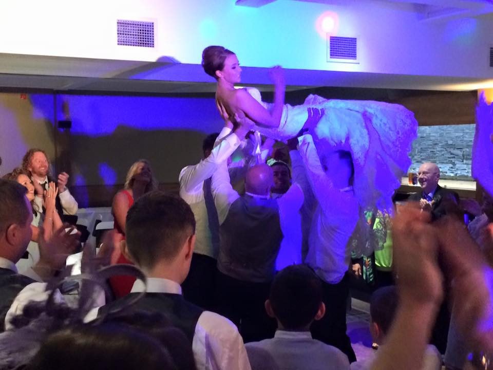 Bride lifted into the air by guests on the dancefloor under blue lighting at a wedding reception