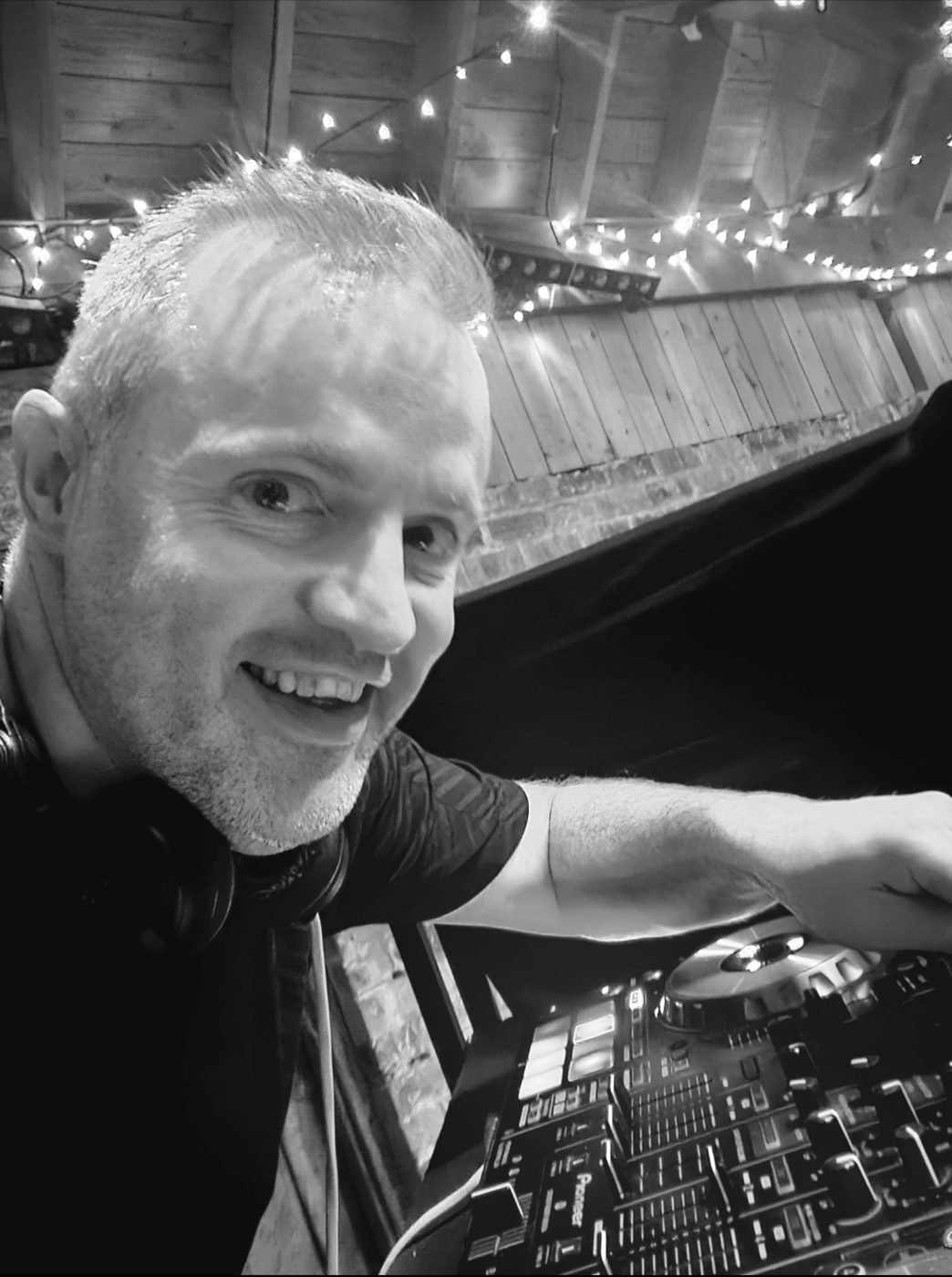 JMD Entertainments DJ mixing at the decks in a barn venue strung with fairy lights